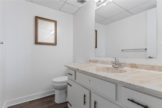 half bath with a paneled ceiling, vanity, toilet, and baseboards