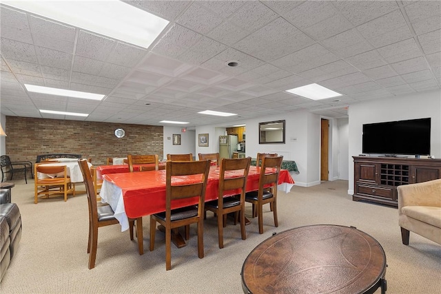 dining area featuring light colored carpet, baseboards, a drop ceiling, and brick wall