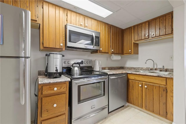 kitchen featuring stainless steel appliances, brown cabinetry, light countertops, and a sink