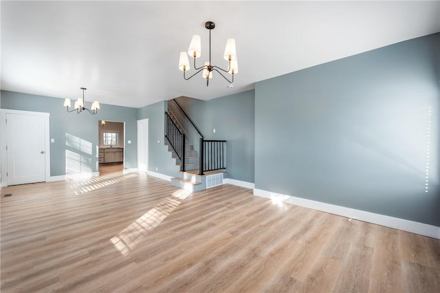 unfurnished living room with light wood-style flooring, a notable chandelier, stairway, and baseboards