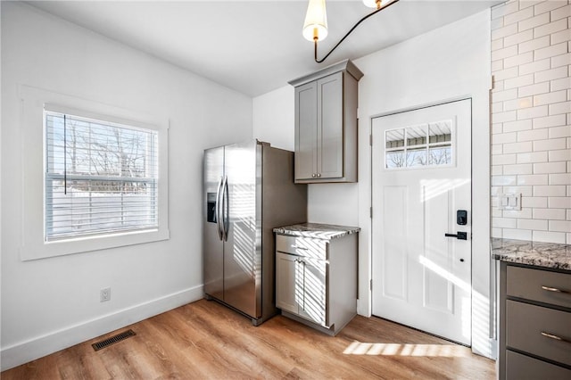 kitchen featuring gray cabinetry, visible vents, light stone countertops, light wood finished floors, and stainless steel fridge