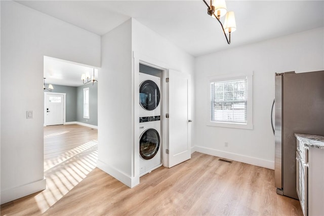 laundry room featuring laundry area, baseboards, light wood-style floors, stacked washing maching and dryer, and a notable chandelier