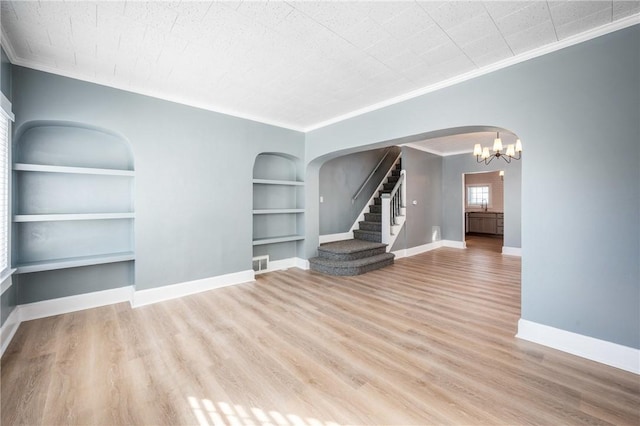 empty room with arched walkways, built in shelves, wood finished floors, visible vents, and baseboards