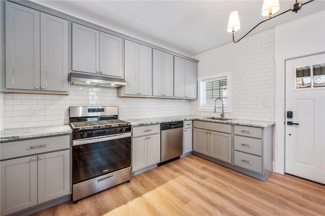 kitchen featuring stainless steel appliances, a sink, light stone countertops, light wood-type flooring, and under cabinet range hood