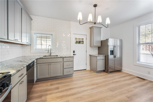 kitchen featuring stainless steel appliances, a sink, hanging light fixtures, and gray cabinetry