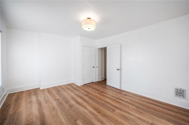 spare room with wood finished floors, visible vents, and baseboards