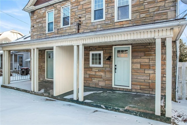 snow covered property entrance with stone siding and covered porch