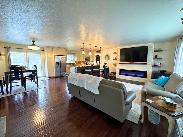 living room with a textured ceiling, dark wood-style flooring, and a glass covered fireplace