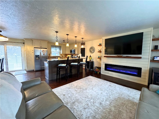 living area with dark wood-style floors, a textured ceiling, and a glass covered fireplace