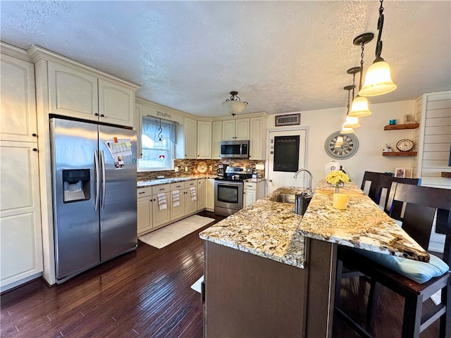 kitchen with cream cabinetry, tasteful backsplash, appliances with stainless steel finishes, dark wood-type flooring, and a sink