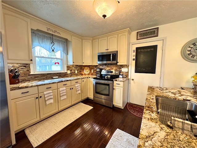 kitchen featuring stainless steel appliances, cream cabinetry, dark wood-type flooring, and light stone countertops