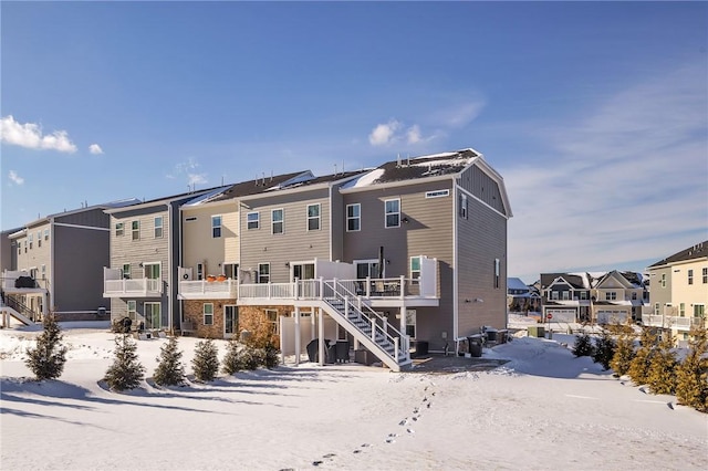 snow covered back of property featuring stairway and a residential view