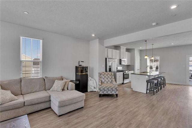 living room with recessed lighting, baseboards, a textured ceiling, and light wood finished floors