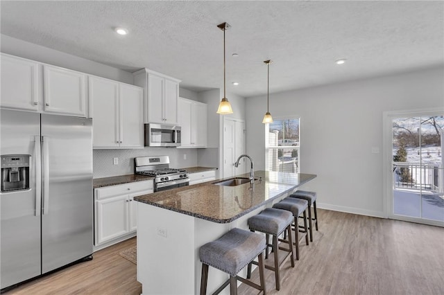 kitchen with appliances with stainless steel finishes, dark stone counters, white cabinets, and a kitchen island with sink