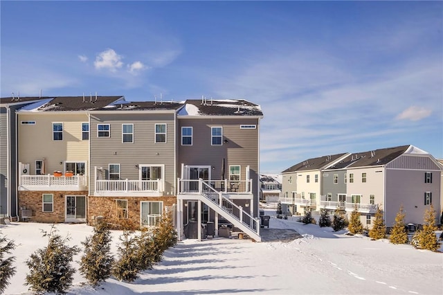 snow covered back of property featuring a residential view, stone siding, and stairs