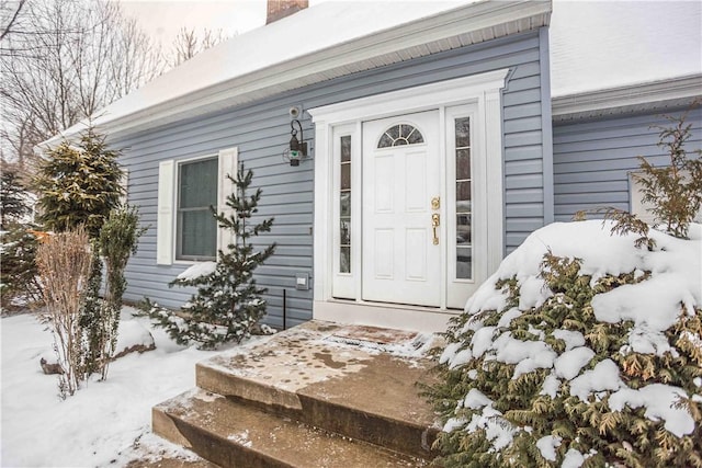 snow covered property entrance with a chimney