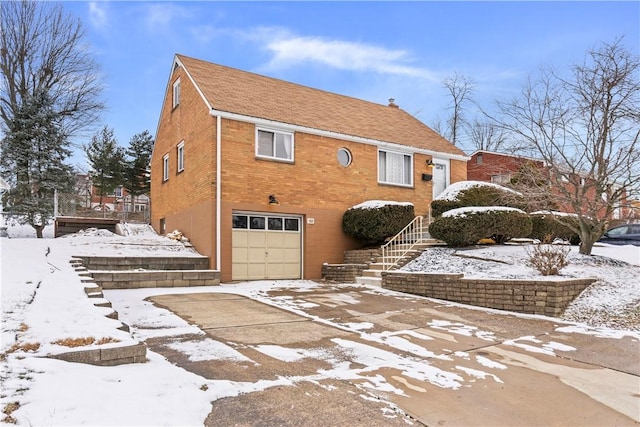 view of snow covered exterior with an attached garage, stairs, and brick siding