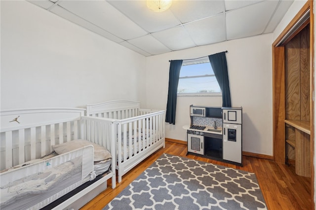 bedroom featuring a drop ceiling, baseboards, and wood finished floors