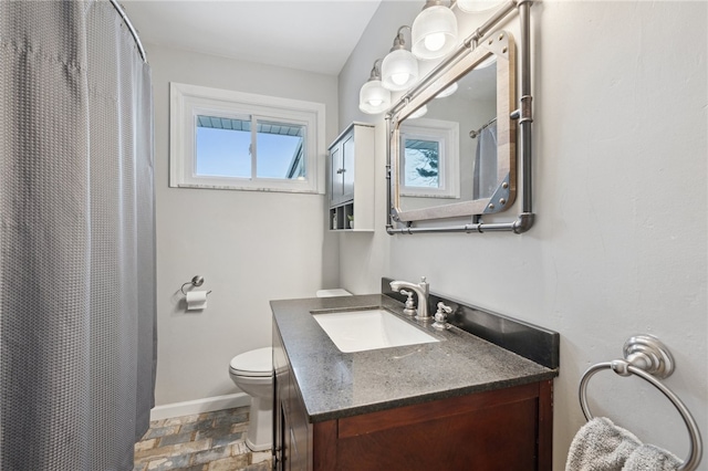 full bathroom with stone finish flooring, toilet, vanity, and baseboards