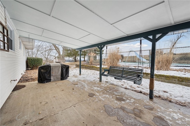 snow covered patio with a grill, fence, and a carport