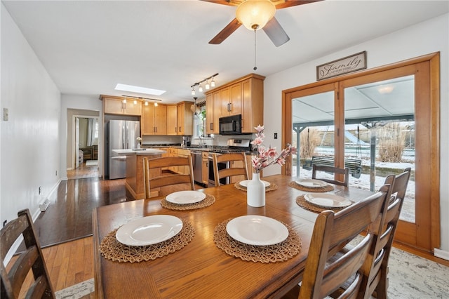 dining area featuring light wood-type flooring, a healthy amount of sunlight, ceiling fan, and a skylight