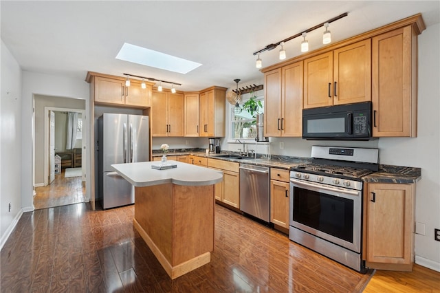 kitchen with a center island, a skylight, appliances with stainless steel finishes, a sink, and wood finished floors