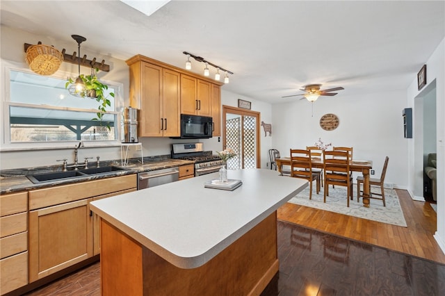 kitchen featuring dark wood-style floors, decorative light fixtures, a center island, stainless steel appliances, and a sink