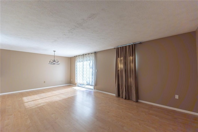 spare room with light wood-type flooring, a textured ceiling, baseboards, and an inviting chandelier