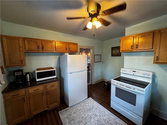 kitchen with white appliances, brown cabinetry, dark countertops, ceiling fan, and dark wood-type flooring