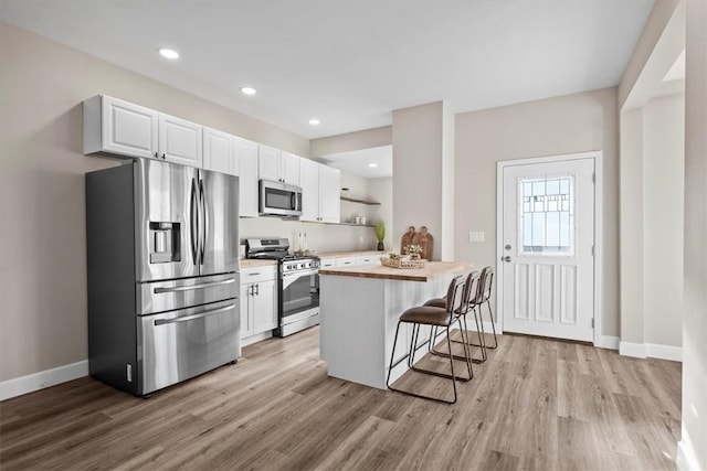 kitchen with a breakfast bar, open shelves, appliances with stainless steel finishes, light wood-style floors, and white cabinets