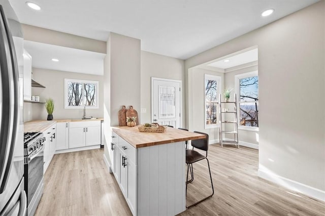 kitchen with light wood-style flooring, wood counters, appliances with stainless steel finishes, a kitchen bar, and white cabinetry