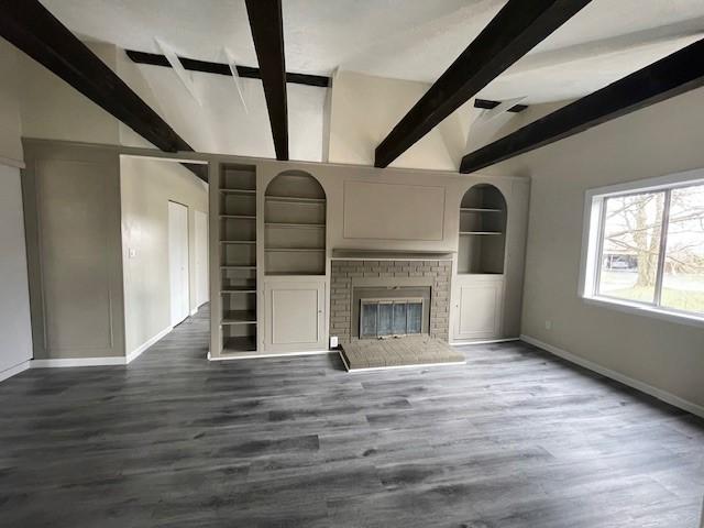 unfurnished living room with baseboards, built in features, dark wood-style flooring, vaulted ceiling with beams, and a fireplace