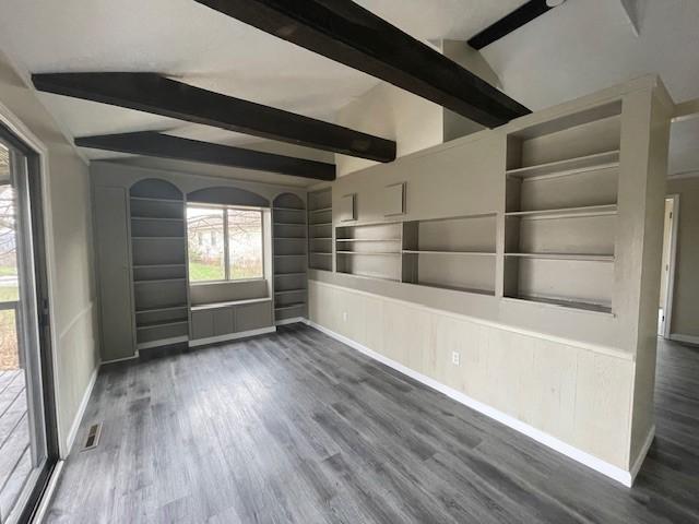 empty room with lofted ceiling with beams, dark wood-style floors, built in shelves, and visible vents