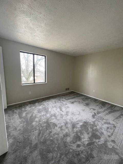 empty room with dark colored carpet, visible vents, a textured ceiling, and baseboards