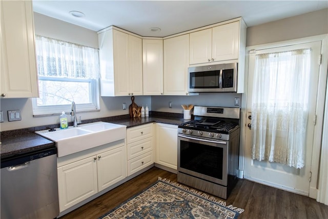 kitchen featuring appliances with stainless steel finishes, dark countertops, white cabinets, and a sink