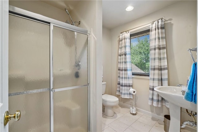full bath featuring baseboards, toilet, a shower with door, tile patterned flooring, and a sink