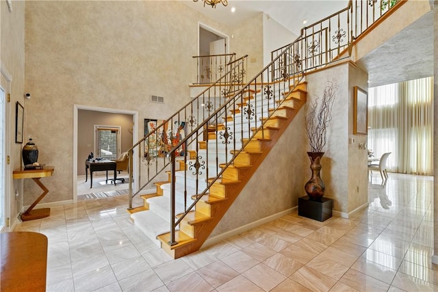 stairs featuring baseboards, a high ceiling, and visible vents