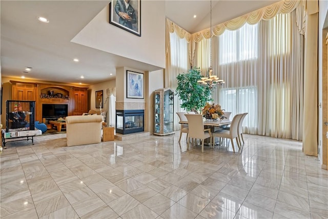 dining space with a towering ceiling, an inviting chandelier, a fireplace, and recessed lighting