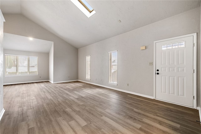 unfurnished living room featuring vaulted ceiling with skylight, baseboards, and wood finished floors