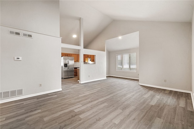 unfurnished living room featuring light wood finished floors, visible vents, and high vaulted ceiling