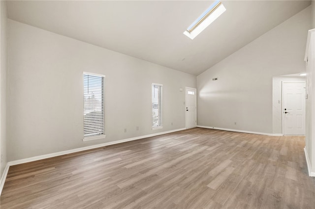 spare room with light wood-style floors, a skylight, high vaulted ceiling, and baseboards