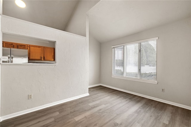 spare room with lofted ceiling, a textured wall, baseboards, and wood finished floors