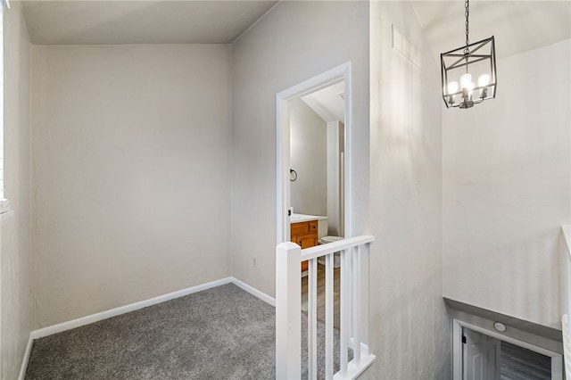 hallway with a chandelier, dark colored carpet, an upstairs landing, and baseboards