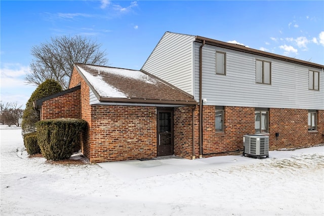 snow covered rear of property with central air condition unit and brick siding