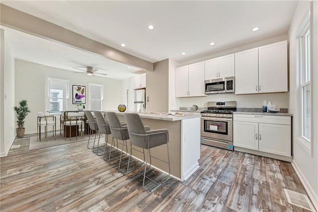 kitchen with stainless steel appliances, visible vents, white cabinetry, light countertops, and a center island with sink