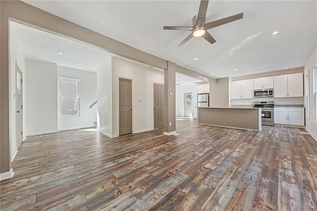 kitchen with an island with sink, appliances with stainless steel finishes, open floor plan, wood finished floors, and white cabinetry