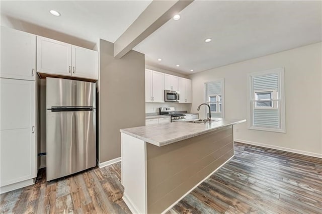 kitchen featuring a center island with sink, stainless steel appliances, white cabinets, a sink, and wood finished floors