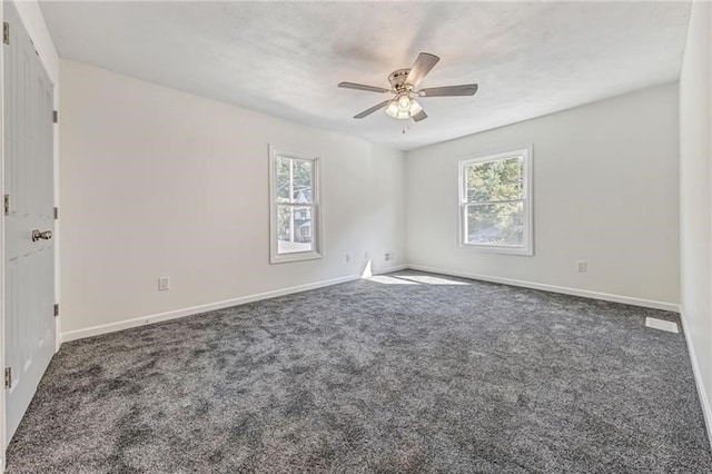 unfurnished room featuring dark colored carpet, a healthy amount of sunlight, ceiling fan, and baseboards