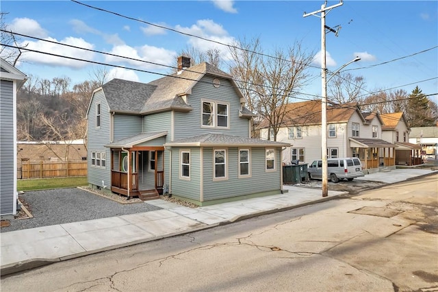 view of front of home with roof with shingles, a chimney, covered porch, fence, and a residential view