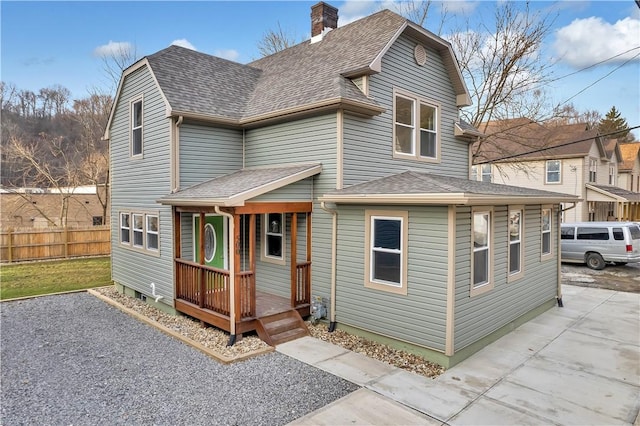 view of front of house featuring a shingled roof, driveway, fence, and a chimney